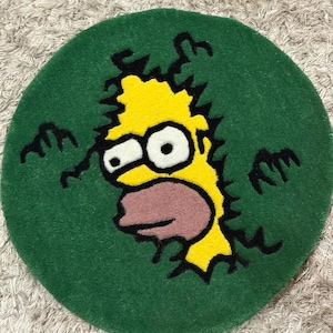 Puede incluir: Una alfombra redonda verde con un personaje de dibujos animados amarillo rompiendo. El personaje tiene grandes ojos blancos y una boca rosa, con contornos negros. La alfombra está sobre una superficie clara y texturizada. Un artículo decorativo.