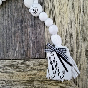 May include: White beaded garland with a black and white checkered ribbon and a white tag that says "Sleeping Baby".