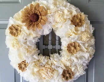 May include: A white and brown burlap wreath with a variety of fabric flowers and lace. The wreath is decorated with brown burlap flowers and white fabric flowers.