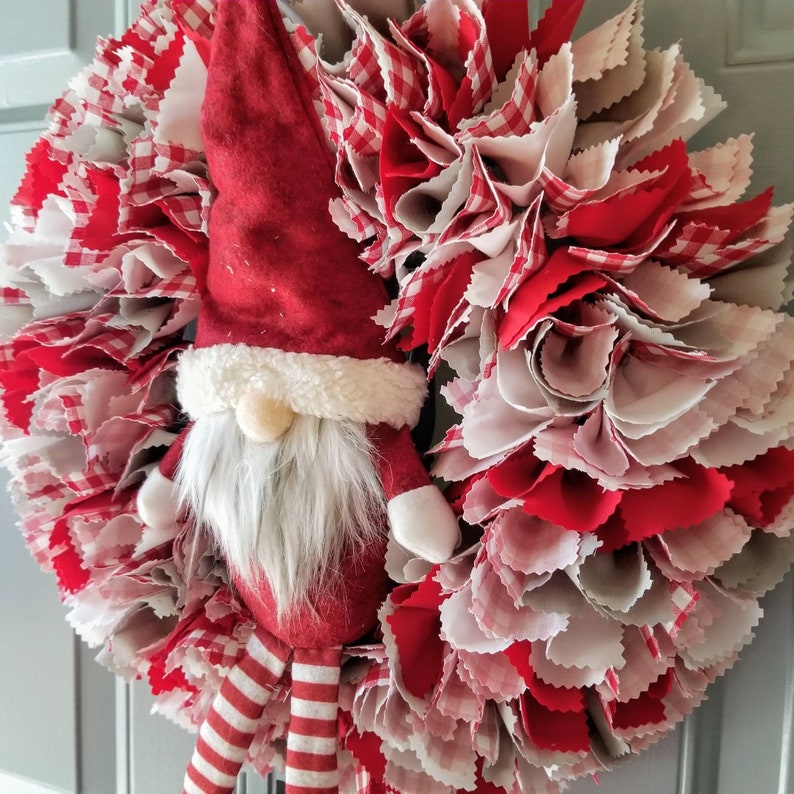 May include: A red and white gingham fabric wreath with a plush gnome wearing a red hat and white beard in the center.