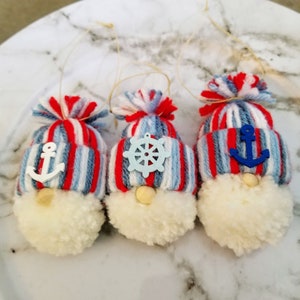 May include: Three handmade gnome ornaments with red, white, and blue striped hats. Each gnome has a different nautical themed embellishment: an anchor, a wheel, and another anchor.