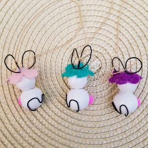 May include: Three white bunny ornaments with wire ears and felt accents. The bunnies have pink, teal, and purple felt accents.