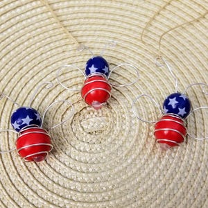 May include: Three wire-wrapped ornaments shaped like bees with red and blue beads. The beads are decorated with white stars.