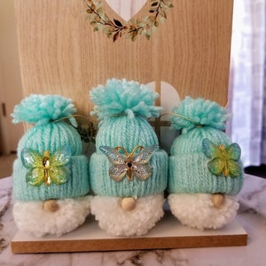 May include: Three small gnomes with white pom-pom beards and blue yarn hats decorated with iridescent butterflies.