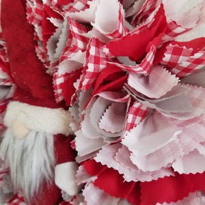 May include: A red and white gingham fabric wreath with a Santa Claus figure in the center. The wreath is made of fabric scraps and is a festive decoration for the holiday season.