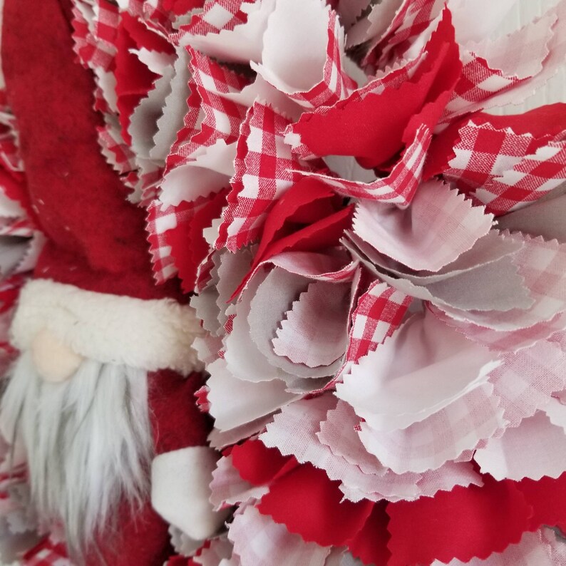 May include: A red and white gingham fabric wreath with a Santa Claus figure in the center. The wreath is made of fabric scraps and is a festive decoration for the holiday season.