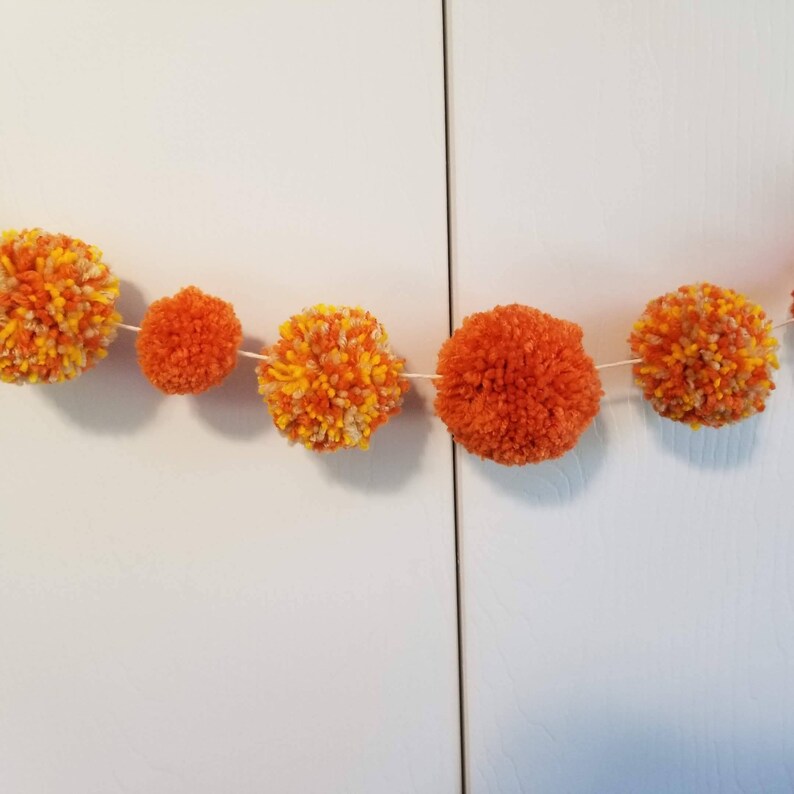 May include: A garland of orange and yellow pom-poms strung together with white thread.