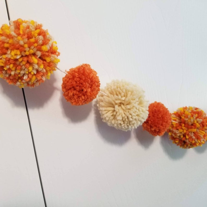 May include: A garland of orange, yellow, and white pom-poms strung together with white thread.