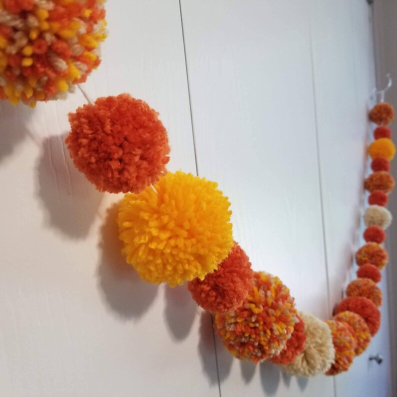 May include: A garland of orange and yellow pom-poms strung together on a white background.
