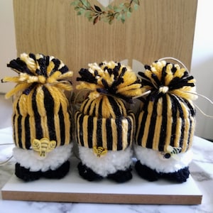 May include: Three small gnomes with black and yellow striped hats and white pom-poms. Each gnome has a small bee button on its hat.