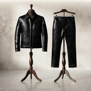 May include: A black jacket and matching trousers set featuring a textured crocodile skin pattern. The jacket has a collared neckline and long sleeves, while the trousers are straight-legged. Both items are displayed on wooden stands.