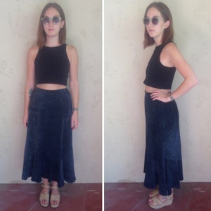 May include: A woman is wearing a black sleeveless crop top and a dark blue denim skirt with a ruffled hem. She is wearing sunglasses and sandals.
