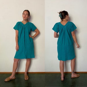 May include: A teal blue, short-sleeved, gathered dress with a V-neckline. The dress is shown on a model wearing it with brown sandals.