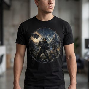 Op de afbeelding: Een zwart t-shirt met korte mouwen en een cirkelvormige grafische print op de borst. Het ontwerp toont een futuristische gepantserde soldaat met een geweer in een gevechtsscène met ruimteschepen, rotsachtig terrein en een grote ring.