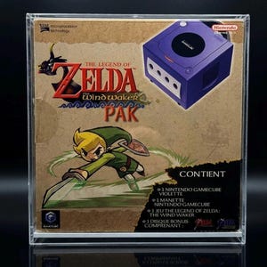 Op de afbeelding: Een Nintendo GameCube The Legend of Zelda The Wind Waker Pak in een doorzichtige acryl displaybox. De doos toont een paarse console, het personage Link en tekst waaronder The Legend of Zelda The Wind Waker Pak en een lijst met inhoud.