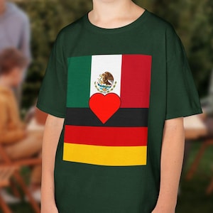 Könnte beinhalten: Ein dunkelgrünes T-Shirt mit einem Grafikdesign, das die Flaggen von Mexiko und Deutschland kombiniert. Das Design umfasst die mexikanische Flagge, ein rotes Herz und die deutsche Flagge. Das T-Shirt wird von einer Person getragen.