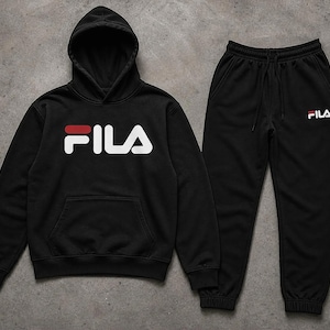 Puede incluir: Conjunto negro de sudadera con capucha y pantal&oacute;n de ch&aacute;ndal Fila. La sudadera con capucha presenta el logotipo de Fila en blanco con un acento rojo. El pantal&oacute;n de ch&aacute;ndal tiene cintura el&aacute;stica y el logotipo de Fila en blanco.