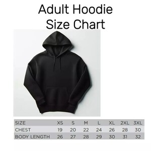 Puede incluir: Sudadera con capucha negra para adultos con una tabla de tallas. La tabla de tallas muestra medidas de pecho de 48 a 76 cm y largos de cuerpo de 66 a 81 cm. La sudadera tiene capucha y bolsillo delantero.