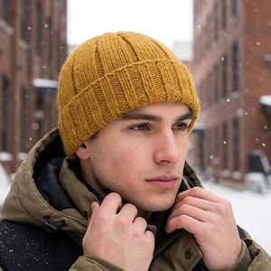 May include: Mustard yellow knit beanie hat. The ribbed knit hat is worn outdoors in a snowy environment. The hat is made of a thick, warm material, perfect for cold weather. The hat is a classic style, suitable for various outfits.