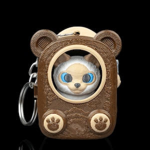 May include: A brown bear-shaped keychain with a white and tan animal face peering through a circular opening. The keychain has a silver ring and a paw print design on the bottom. The background is black.