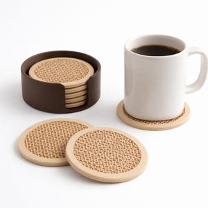 May include: A set of beige and brown coasters with a textured surface, displayed with a white mug of coffee and a brown coaster holder. The coasters have a light beige border and a textured center.