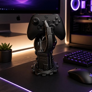 Könnte beinhalten: Ein schwarzer Gaming-Controller ruht auf einem detaillierten, metallischen, handförmigen Ständer. Der Ständer hat eine zahnradartige Basis und komplizierte mechanische Details. Das Setup befindet sich auf einem schwarzen Schreibtisch.