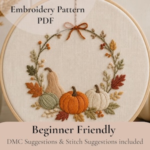 May include: An embroidery pattern PDF featuring a circular wreath design on off-white fabric within a wooden hoop. The wreath includes embroidered pumpkins, autumn leaves, and berries in orange, green, and tan. Text reads: Embroidery Pattern PDF, Beginner Friendly, DMC Suggestions & Stitch Suggestions included.