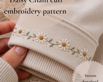 May include: Close-up of a beige sweatshirt cuff featuring a daisy chain embroidery pattern. The cuff is adorned with embroidered daisies in white and yellow, with green leaves. The text "Daisy Chain cuff embroidery pattern" is visible.