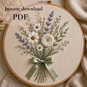 以下が含まれることがあります： 木製のフレームに刺繍された花の模様。白いデイジー、ラベンダー、中央のバラが特徴で、すべて緑色のサテンリボンで結ばれています。「Instant download PDF」の文字が上部に表示されています。