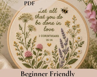 May include: An embroidery pattern PDF featuring a circular hoop with cream fabric. The design includes green stems, pink clover, white wildflowers, lavender, a small bee, and a gold heart. Text reads: Let all that you do be done in love 1 CORINTHIANS 16:14.