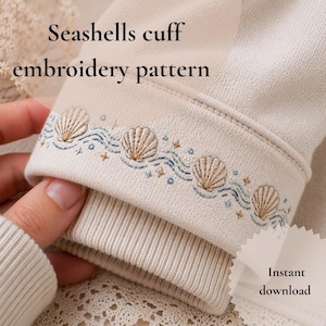 Könnte beinhalten: Nahaufnahme eines beigefarbenen Sweatshirt-Bündchens mit Muschelstickerei. Das Design zeigt gestickte Muscheln, blaue Wellen und kleine Sternakzente. Der Text "Seashells cuff embroidery pattern" ist sichtbar.