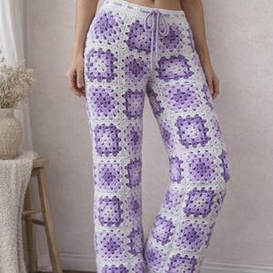 May include: Crocheted pants in a granny square pattern, featuring a combination of white and lavender squares. The pants have a drawstring waist and a relaxed fit, perfect for casual wear. The crochet work is detailed and visually appealing.