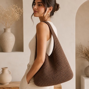 May include: A brown crochet shoulder bag with a long strap. The bag is made of a textured, woven material and is worn over the shoulder. The bag is a solid color and appears to be empty.