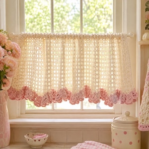 May include: Cream-colored crochet window valance with a pink scalloped edge. The valance is hung on a white rod in front of a window. The crochet pattern is open, allowing light to filter through. A vase of pink flowers is on the left.