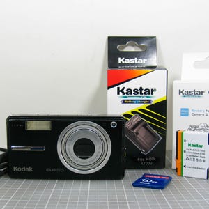 May include: A black Kodak digital camera with a silver lens, a blue SD card, and Kastar camera accessories, including a battery charger and battery pack. The camera has a 6.1-megapixel resolution.