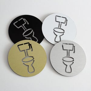 May include: Four circular toilet signs in black, white, gold, and silver. Each sign has a cut-out outline of a toilet. These signs are designed for use in restrooms and are suitable for various decor styles.