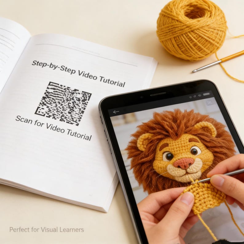May include: A tablet displays a crochet lion tutorial, with a ball of yellow yarn and a crochet hook nearby. A book with the text "Step-by-Step Video Tutorial" and a QR code is open next to the tablet. The image shows a crochet project in progress.