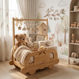 May include: A light-colored wooden carriage-shaped storage organizer featuring a bow, a hanging mobile with stars and moons, a teddy bear, a plush rabbit, a baby onesie with a bear graphic, a book labeled My Little Book, and a sign saying Hello.