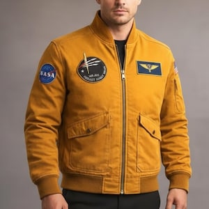 May include: Mustard-colored bomber jacket with a zip-up front, two front pockets, and ribbed cuffs and hem. Features NASA and other patches on the chest and sleeves. A stylish, casual jacket.