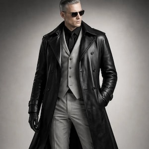May include: A long black leather trench coat with a double-breasted design. The coat is worn over a grey waistcoat and trousers, with a black shirt and gloves. The person is wearing sunglasses.