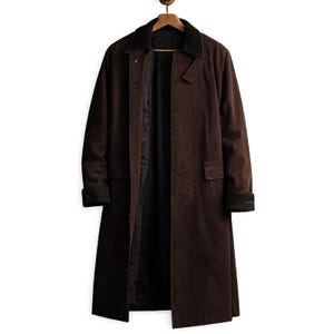 May include: A long brown coat with a black collar and cuffs hangs on a wooden hanger. The coat has a button-up front, two front pockets, and a black interior lining. The coat is made of a durable material and is suitable for cooler weather.