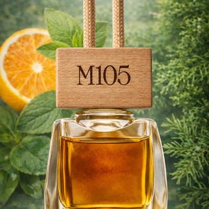 Peut inclure: Flacon en verre transparent rempli de liquide ambré, surmonté d'un bloc de bois gravé "M105". Le flacon est suspendu à deux cordons beiges. Une tranche d'orange et des feuilles vertes sont en arrière-plan. Le texte "Orange BIO", "Mint BIO", et "Cypress BIO" est en bas.