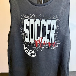 May include: Black tank top with the words "SOCCER Mom" in white and red glitter lettering. A soccer ball graphic with a white trail is on the left side. The text is surrounded by small silver rhinestones.