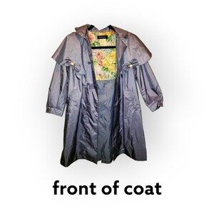May include: A vintage, blue-gray raincoat with a cape-like overlay and bow accents. The interior lining features a floral pattern with pink and yellow roses. The coat has a classic design with a button closure and long sleeves.