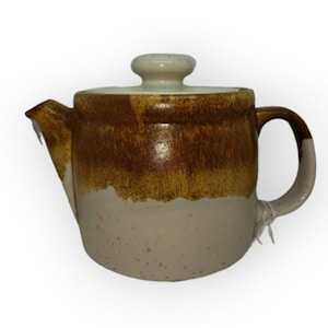 May include: A ceramic teapot with a lid and handle. The teapot is primarily cream-colored with a brown band around the middle and a brown top. The handle and lid knob are cream-colored. The teapot has a spout for pouring.