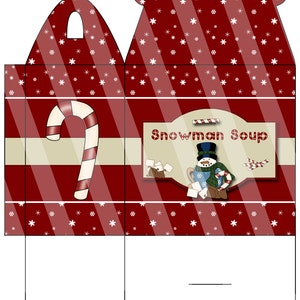 Peut inclure: Une boîte rouge et blanche à rayures avec une poignée, décorée de flocons de neige. Le devant de la boîte représente un bonhomme de neige tenant une tasse de chocolat chaud et le texte "Snowman Soup".