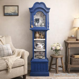 May include: A tall, blue cabinet with glass doors and shelves, displaying various decorative items. The cabinet has a floral wallpaper backing and is painted in a deep blue color. The cabinet is approximately 60 inches tall.