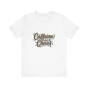 May include: White t-shirt with the text "Caffeine and Chaos" in a brown and teal script. The shirt is a casual style, suitable for everyday wear.