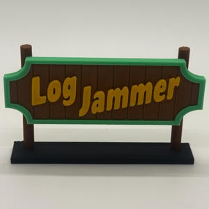 May include: A brown sign with the words "Log Jammer" in yellow, framed by a green border. The sign is supported by two brown posts and a black base, creating a miniature decorative piece.