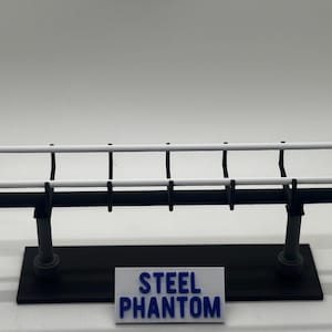 May include: A black and white model of a billboard with the text "STEEL PHANTOM" on a small sign at the base. The billboard has two white horizontal bars and black supports.